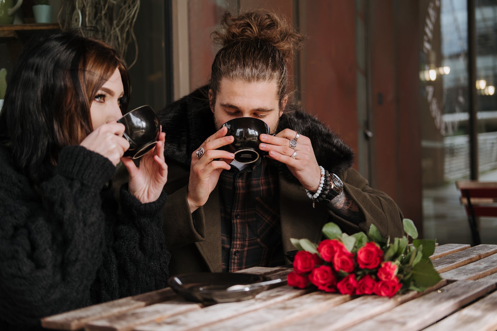 couple enjoying delicious coffee at cafe table with blossoming roses
